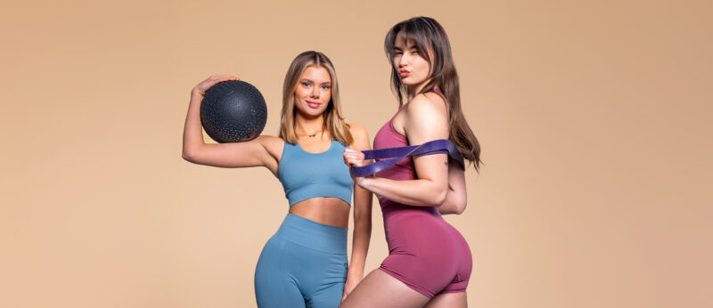Two women in sports attire with a ball and a resistance band - a symbol of the balance between training and proper nutrition.