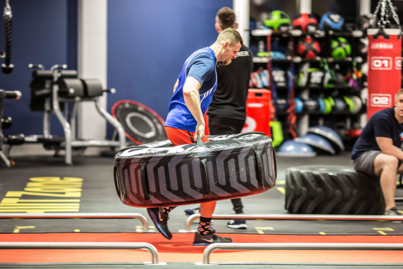 A man performing a functional workout with a tyre at Just Gym Lublin - a HIIT zone with a red track and modern equipment.