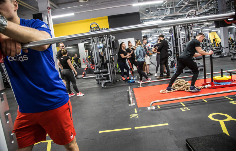 Strength training at Just Gym Lublin - participants performing functional and strength exercises on the red training track.
