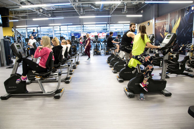 The cardio zone at Just Gym Lublin - people exercising on Matrix stationary bikes in a modern, spacious interior.
