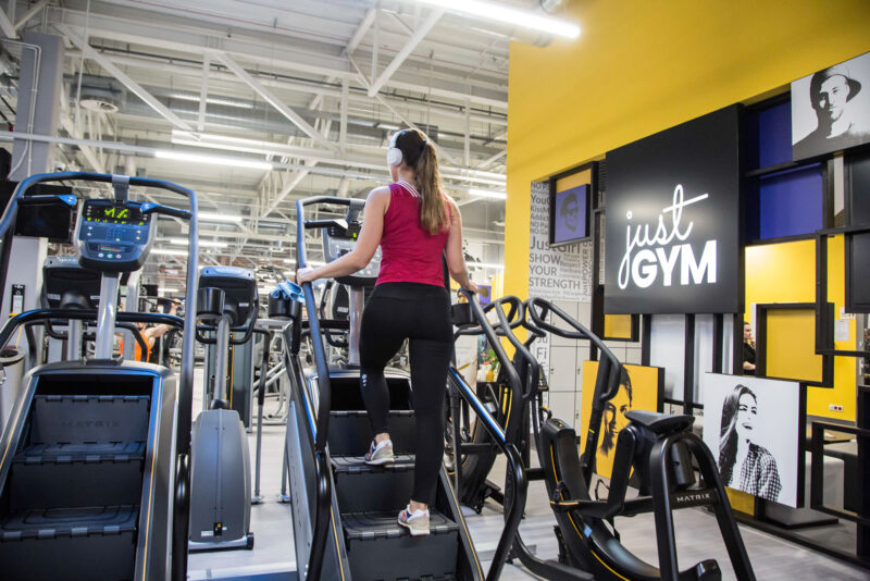 A female trainer on the training steps at Just Gym Lublin - a cardio zone with modern equipment and the club's distinctive yellow and black décor.