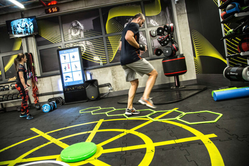 Trening funkcjonalny w siłowni Just Gym Kraków – uczestnicy wykonują ćwiczenia z wykorzystaniem sprzętu interaktywnego w strefie treningu digital fitness.