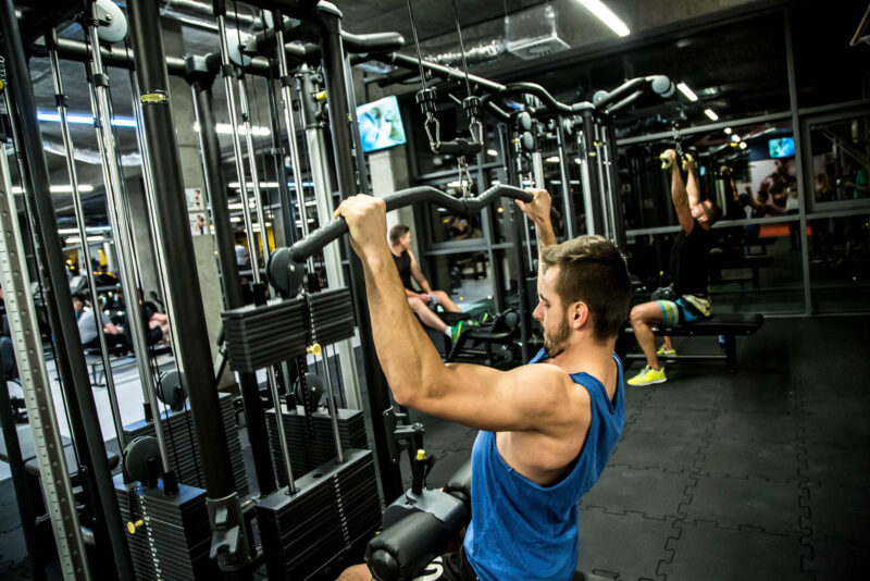 Mężczyzna trenujący na maszynie do ściągania drążka w siłowni Just Gym Kraków – strefa maszyn siłowych.