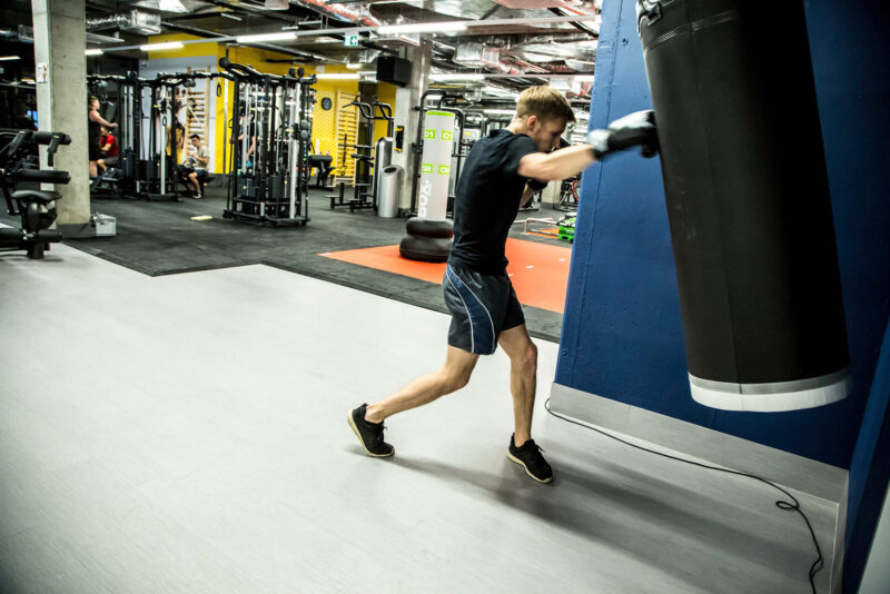 Trening bokserski w siłowni Just Gym Kraków – mężczyzna uderzający w worek bokserski w przestronnej sali treningowej.