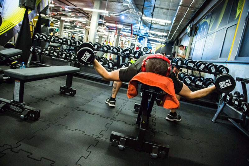 Mężczyzna ćwiczący z hantlami w strefie wolnych ciężarów siłowni Just Gym Kraków – trening na ławce z lustrami w tle.