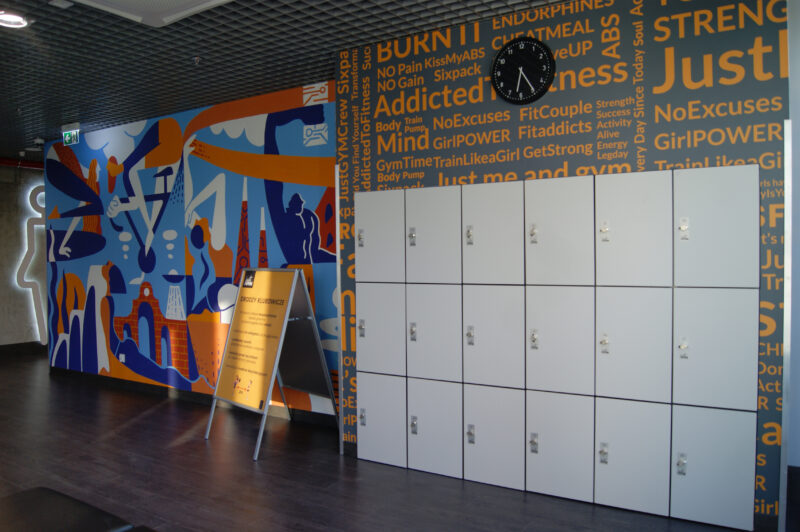 The entrance area at Just Gym Łódź Piotrkowska - a colourful wall with graphics, lockers and the club's motivational sign.