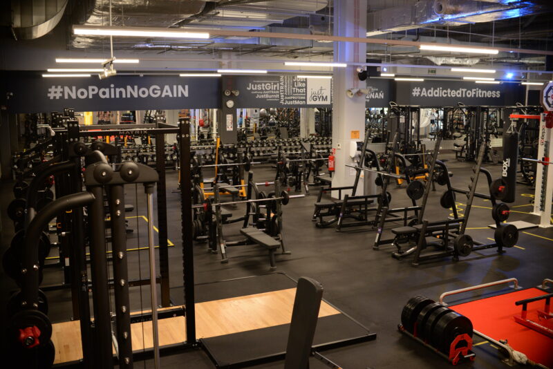 Just Gym Poznań Bulgarska free weights zone - workout stations with motivational slogans #NoPainNoGain and #AddictedToFitness.