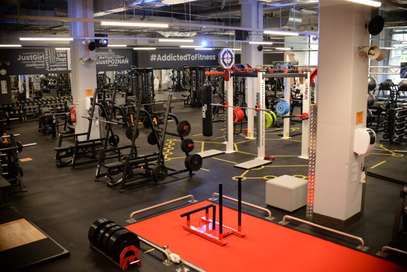 Just Gym Poznań Bulgarska training space - red track, dumbbells, punching bags and squat stations.