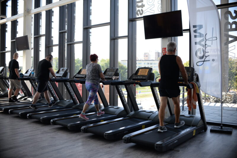 Strefa cardio w siłowni Just Gym Jastrzębie-Zdrój – osoby ćwiczące na bieżniach przy dużych przeszklonych oknach z widokiem na miasto.