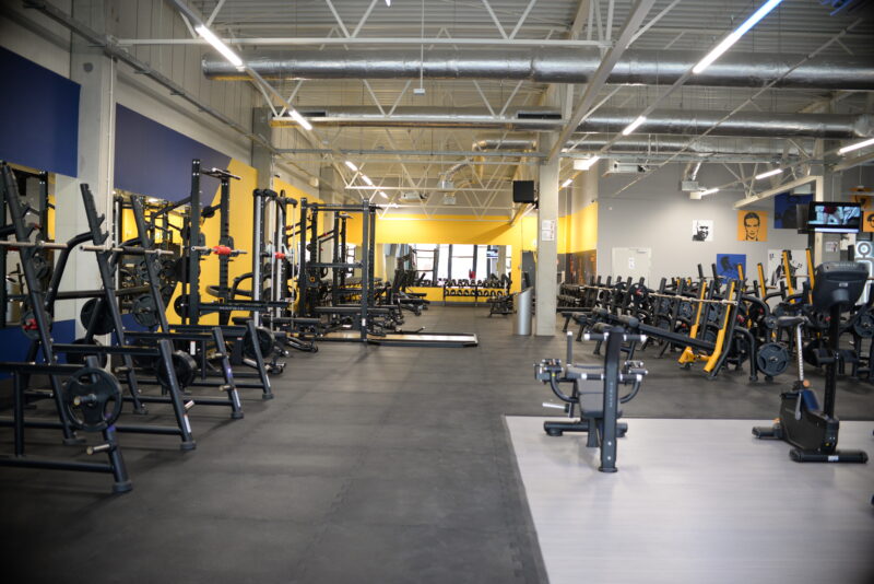 Just Gym Slupsk free weights zone - a spacious room with strength machines and yellow and blue decor.