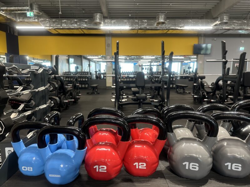Kettlebells w różnych kolorach w strefie wolnych ciężarów Just Gym Tychy – sprzęt fitness i lustra treningowe.