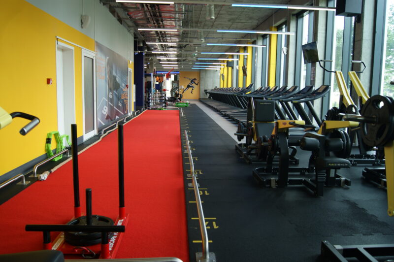The red functional track and treadmill area of Just Gym Warsaw Mokotów - a spacious interior with yellow accents.