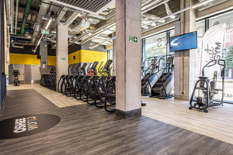 Сучасна кардіо-зона у Just Gym Wrocław з тренажерами Matrix на тлі скляних стін та телевізійних екранів.