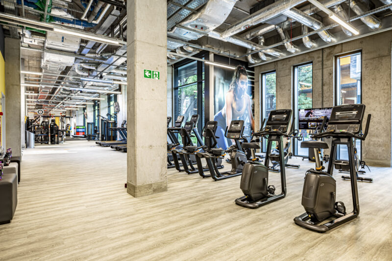 Просторий тренажерний зал Just Gym Wrocław зі стаціонарними велотренажерами, біговими доріжками та великим спортивним муралом.