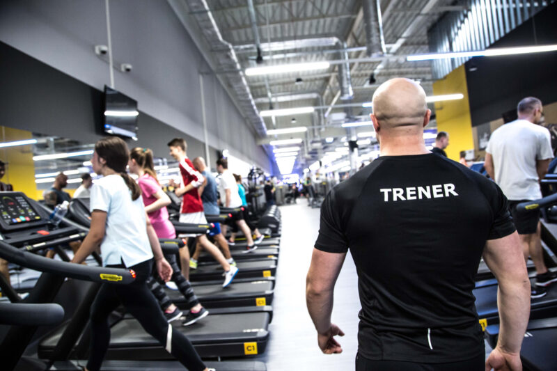 Just Gym Poznan Swiss trainer supervising exercises in the cardio zone - treadmill users during training.