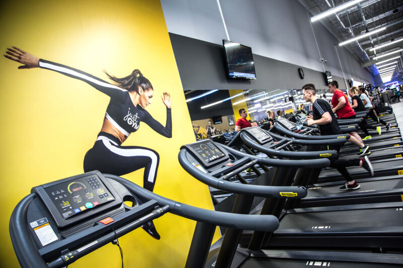 Just Gym Poznań Swiss cardio zone - Technogym treadmills with distinctive yellow graphics on the wall.