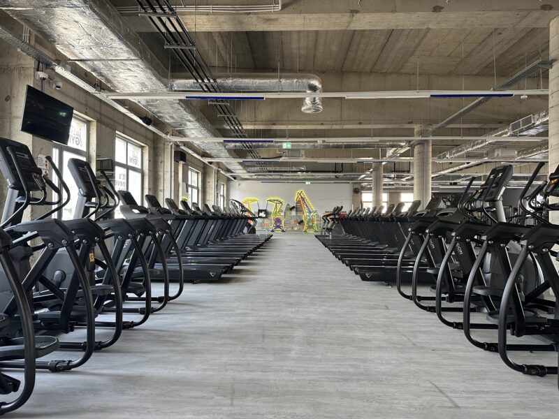 Just Gym Szczecin cardio zone - a row of treadmills and orbiters in a bright, modern club interior.