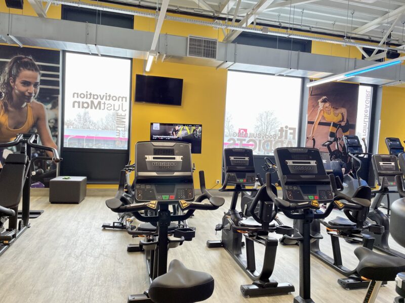 Stationary bike zone at the Just Gym Gniezno - a cardio training space with panoramic windows and yellow accents.