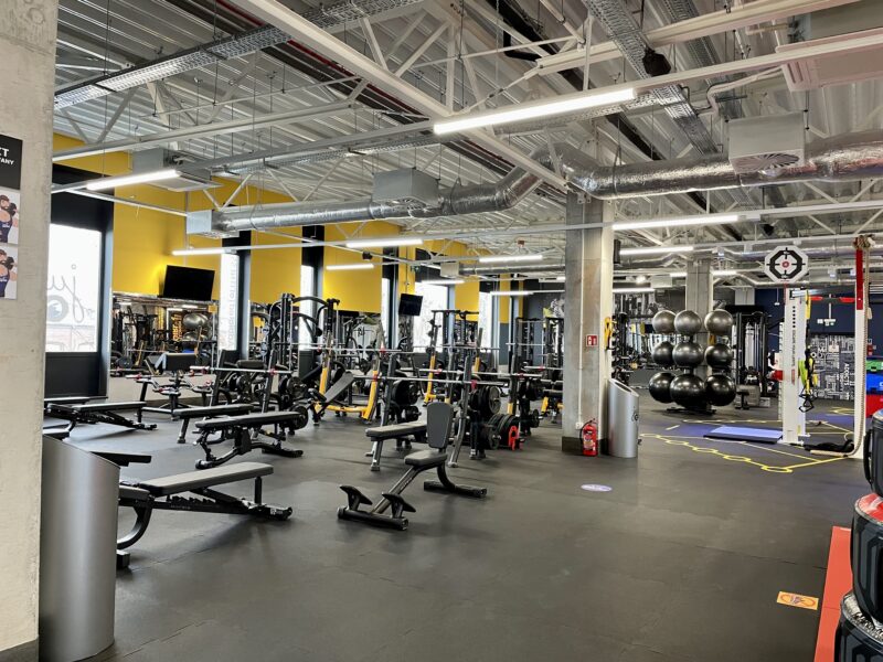 The modern training area of the Just Gym Gniezno gym with benches, strength machines and free weights in a spacious interior.