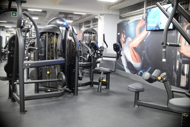 Nowoczesna sala treningowa Just Gym Łódź Rewolucji z maszynami do ćwiczeń i grafiką motywacyjną na ścianie.