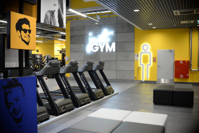 The cardio zone at Just Gym Pabianice - a row of modern Matrix treadmills in a bright, airy interior with yellow accents.