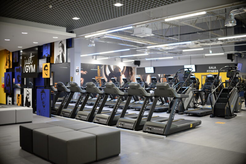 Modern orbiters and treadmills at Just Gym Pabianice - a cardio training space with fitness graphics on the wall.