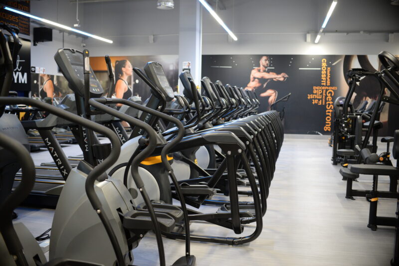 The cardio zone at Just Gym Pabianice - Matrix treadmills and orbiters in a modern gym with a fitness room in the background.