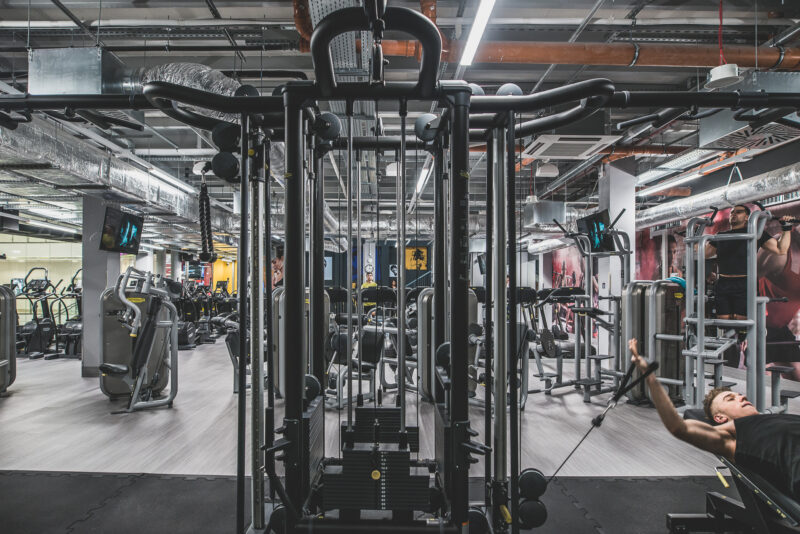 Strefa maszyn w siłowni Just Gym Elbląg – widok na urządzenia do treningu siłowego i wyciągi linowe.