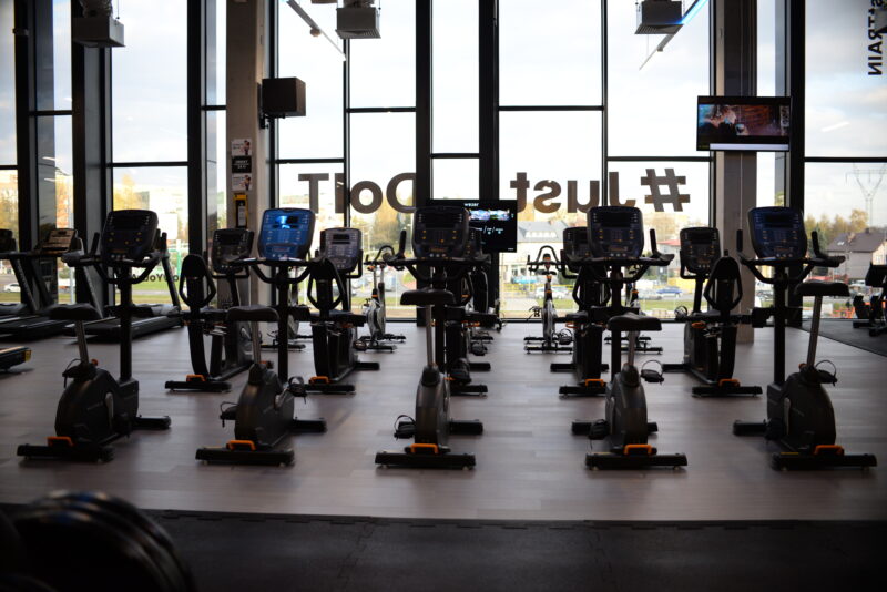 Strefa rowerków stacjonarnych w siłowni z panoramicznymi oknami i widokiem na miasto.