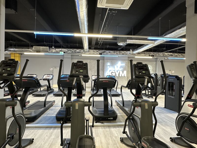 The cardio zone in the Just Gym Częstochowa gym with treadmills and orbiters arranged in rows, against a modern interior with the club's logo on the wall.