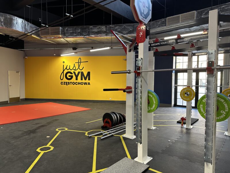 Workout area in the Just Gym Częstochowa gym with the club's logo visible on the yellow wall, a pull-up structure and Escape Your Limits weights.