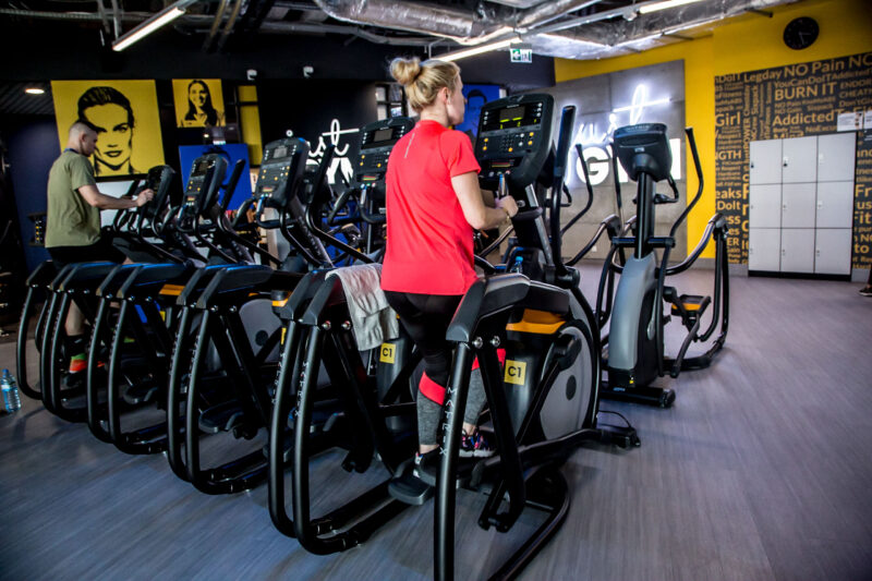 Treadmills and orbiters at Just Gym Opole - a colourful gym interior with a yellow accent and „Just Gym Opole” sign.
