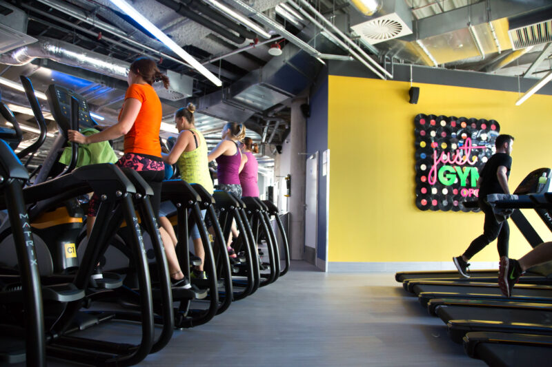 The cardio zone in the Just Gym Opole gym - Matrix treadmills and orbiters against a yellow wall with the club's logo.