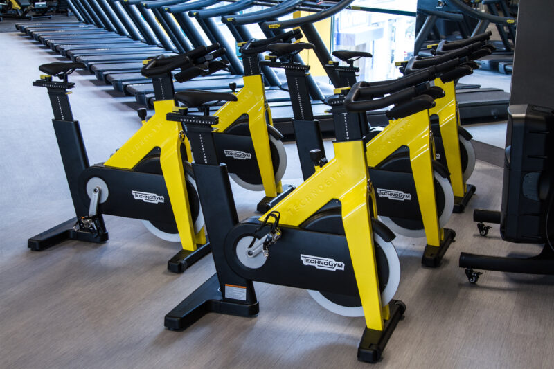 Spinning bike zone in the Just Gym Plock gym - yellow and black Technogym bikes in a modern club interior.