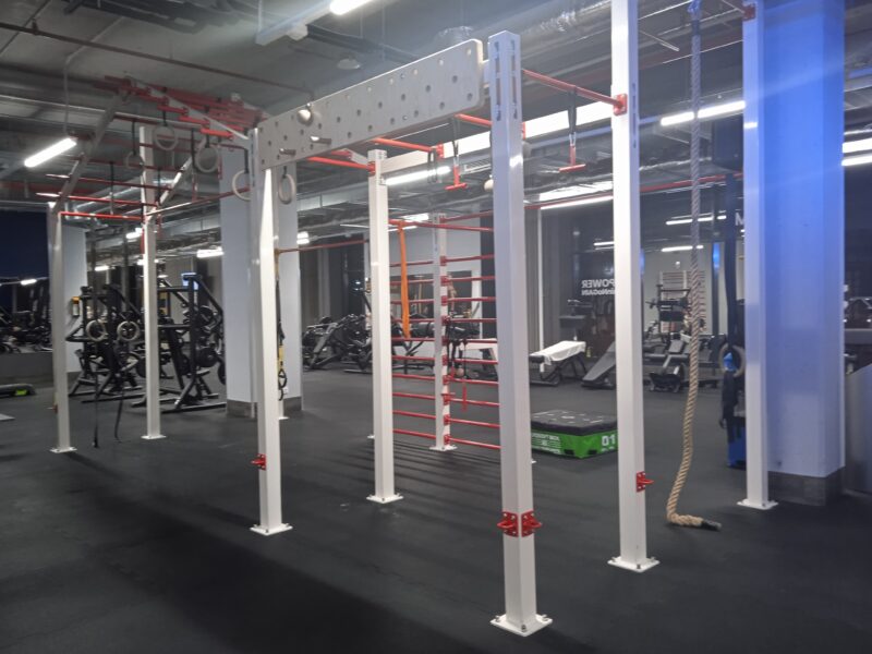 Functional training area with a pull-up structure, rope and gymnastic wheels, with strength equipment in the background.