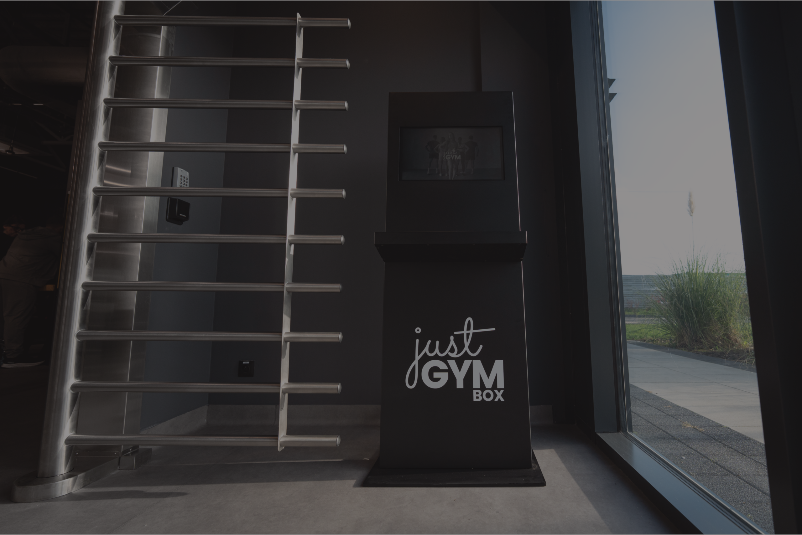 Entrance gate and self-service reception at Just Gym Box Warsaw - turnstile, terminal with club logo at glass entrance.